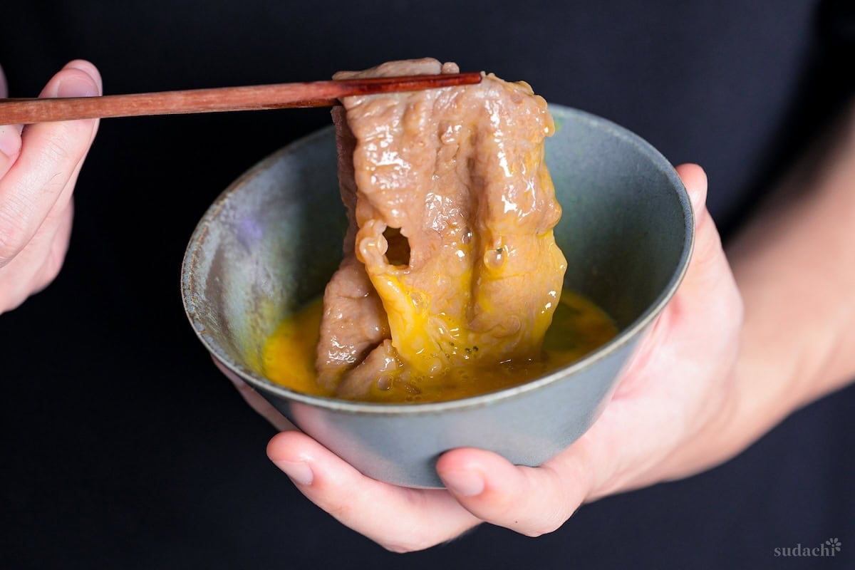 Yuto Omura holding up a piece of sukiyaki beef dipped in raw egg