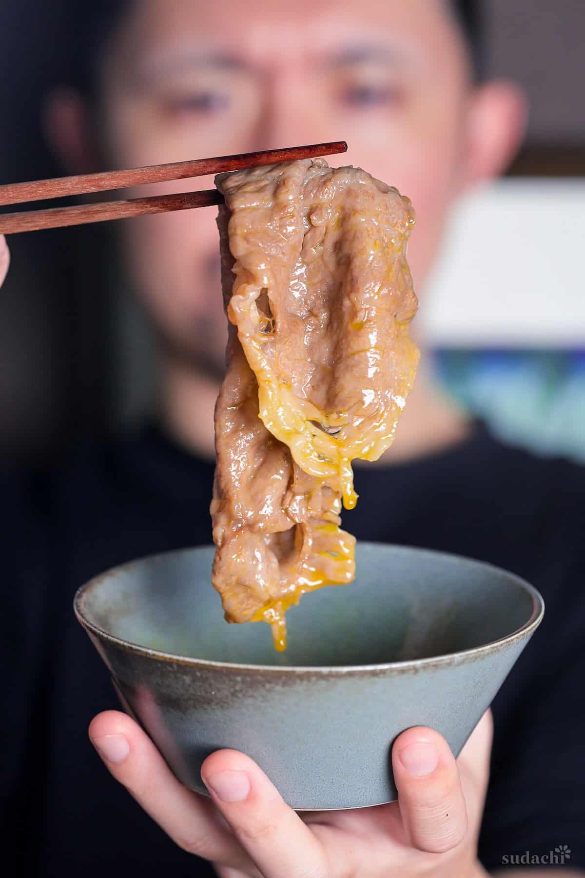 Yuto Omura holding up a piece of sukiyaki beef dipped in raw egg