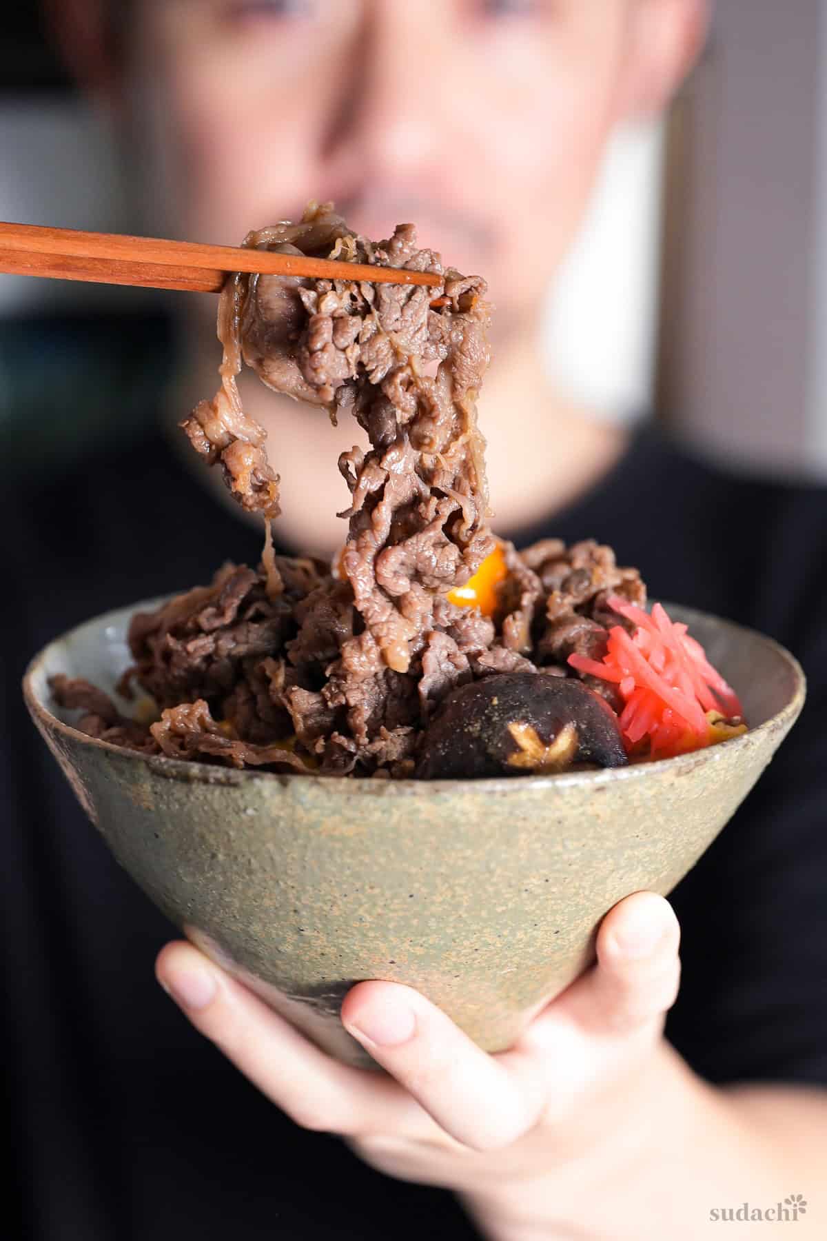Yuto Omura holding up a piece of cooked thinly sliced beef over a bowl of sukiyaki don