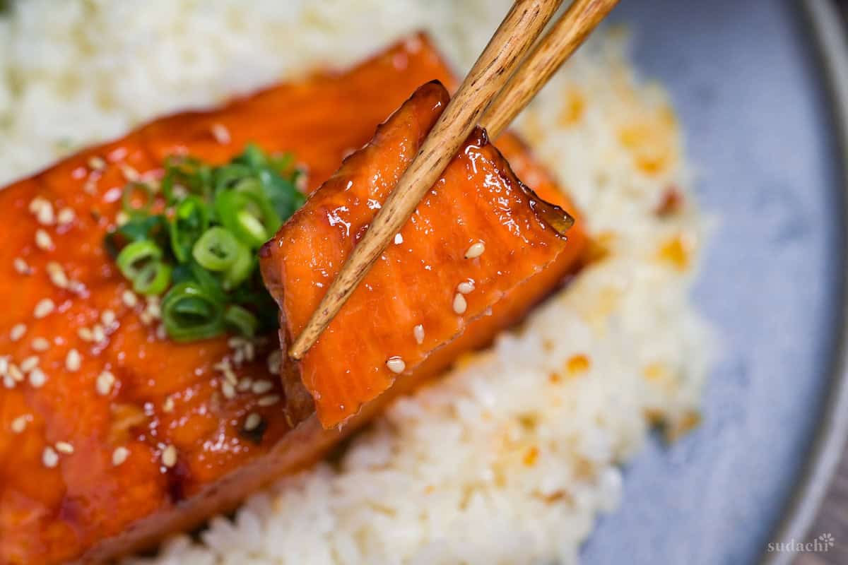 close up of a piece of teriyaki salmon held up with wooden chopsticks