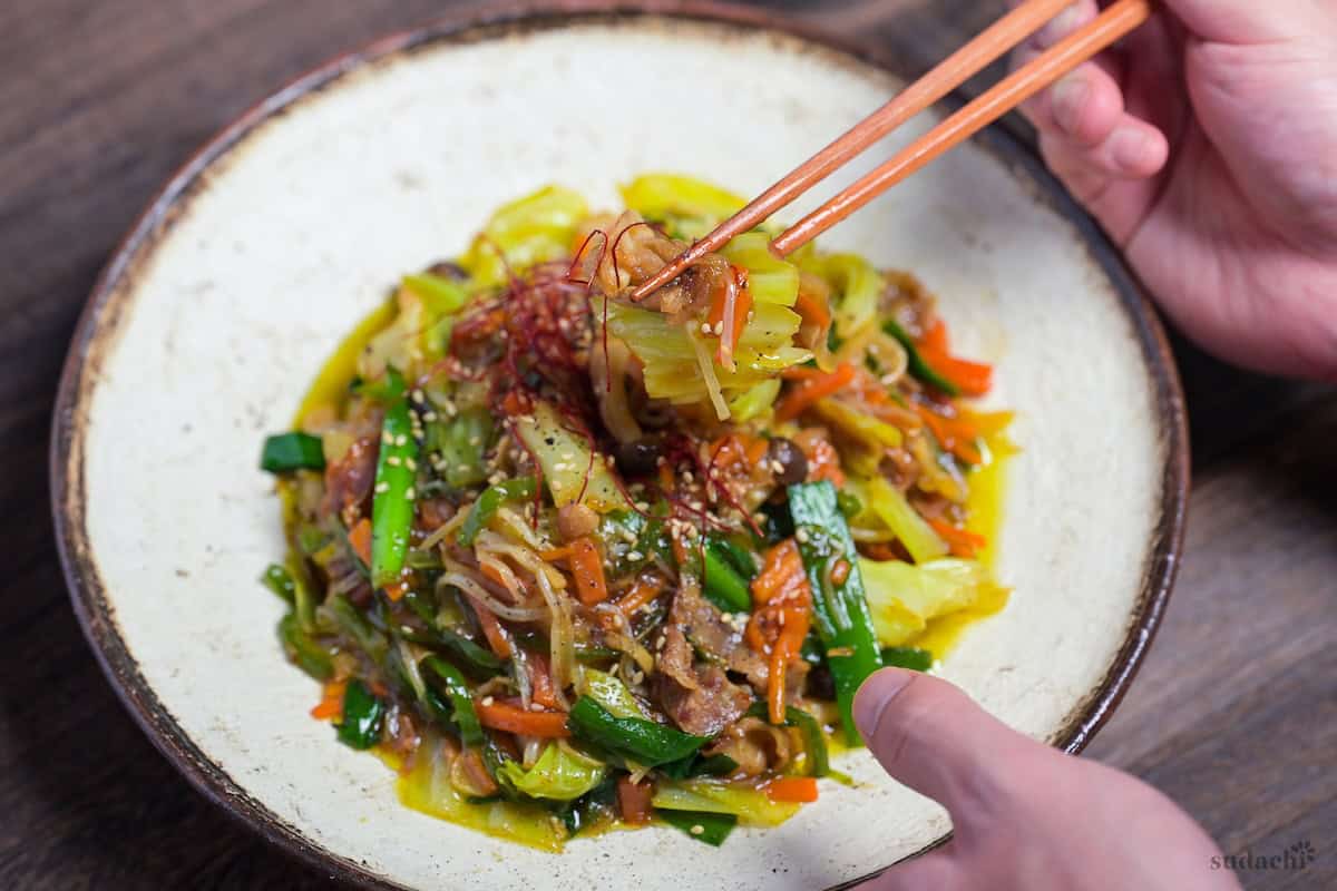 Niku Yasai Itame (Japanese meat and vegetable stir fry) topped with chili threads and sesame seeds on a cream plate with brown rim.