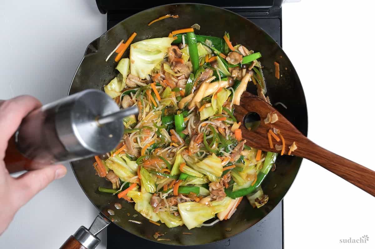 Drizzling niku yasai itame in a wok with toasted sesame oil.