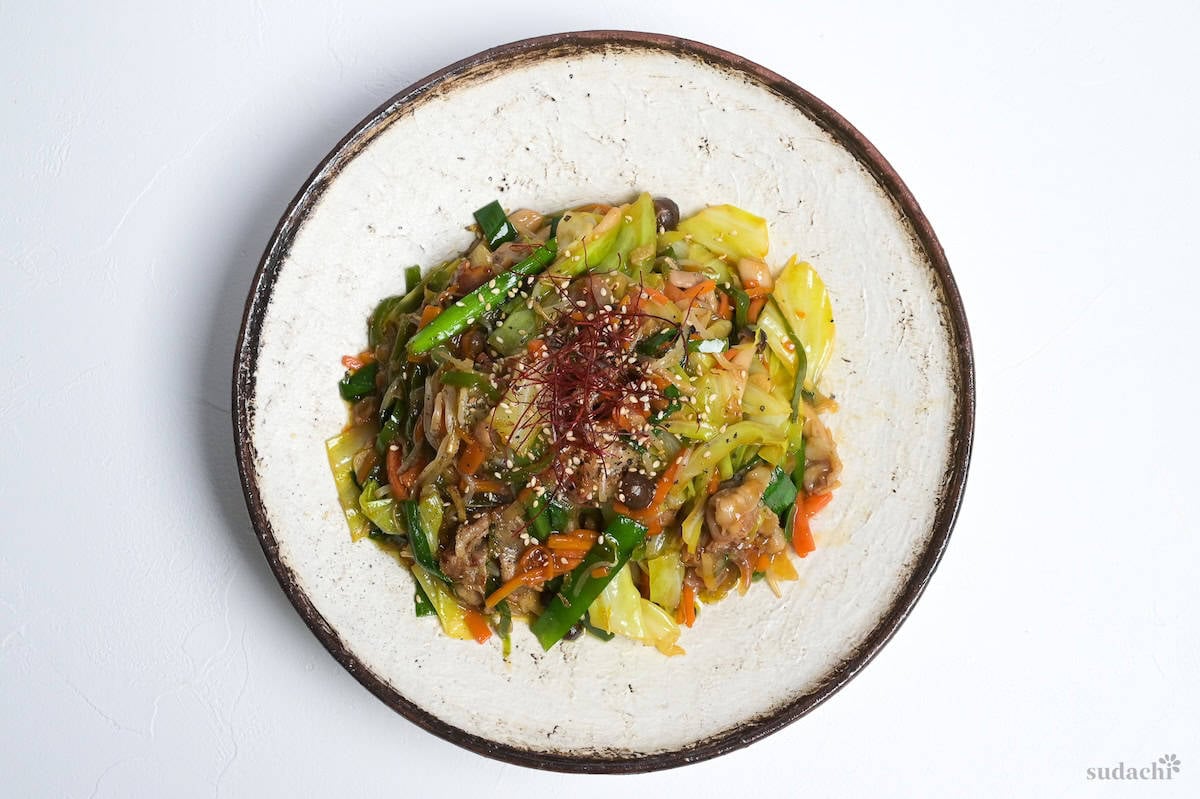 Niku Yasai Itame (Japanese meat and vegetable stir fry) topped with chili threads and sesame seeds on a cream plate with brown rim.
