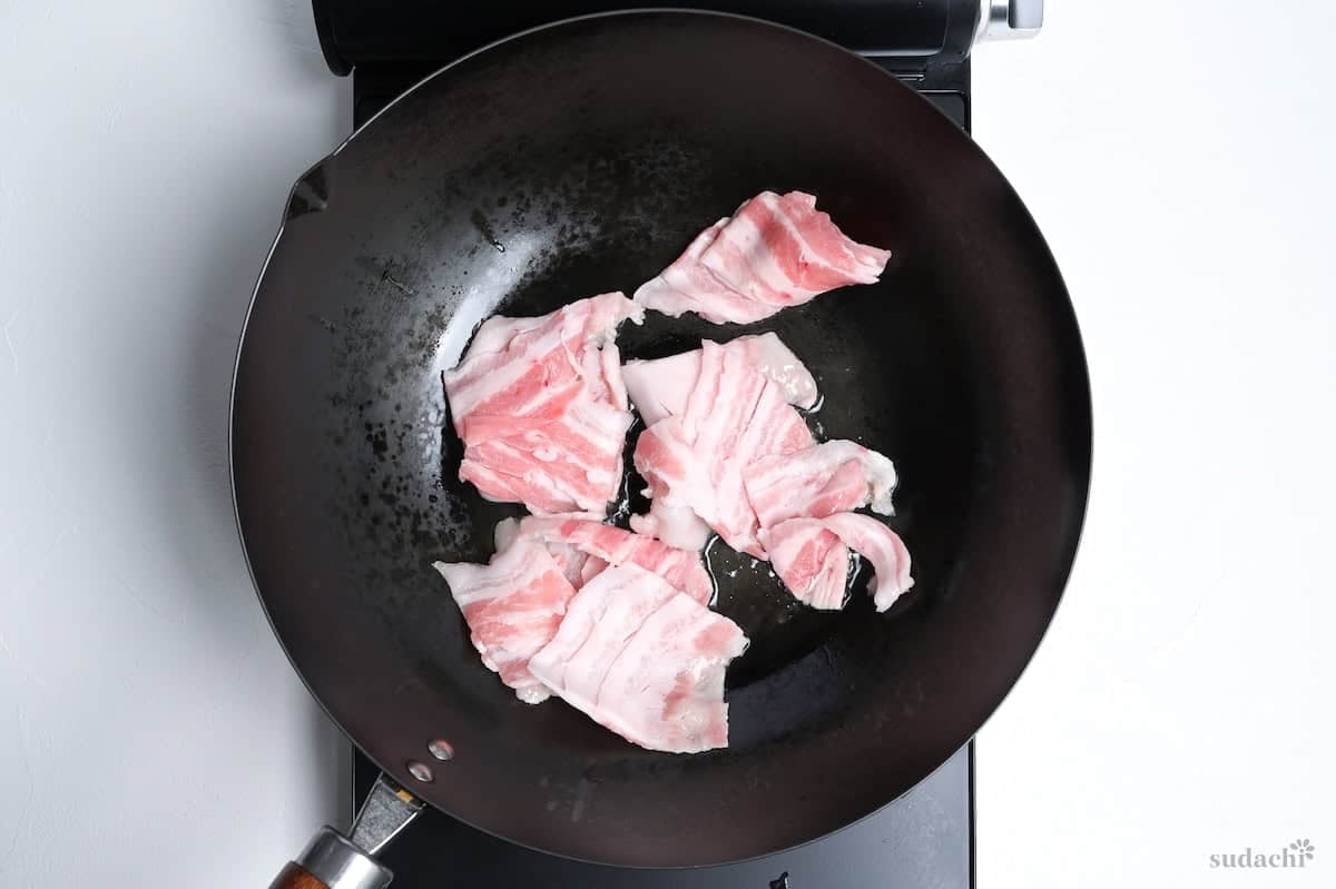 Thinly sliced pork frying in a wok on the stove top.