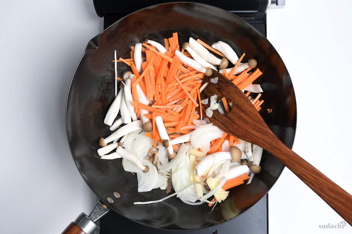 onion, mushrooms, carrot and garlic frying in a wok on the stove top.