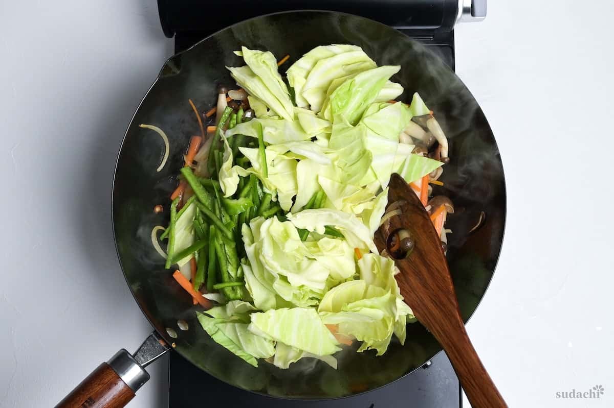 cabbage and green bell peppers added to niku yasai itame frying in a wok on the stove top.