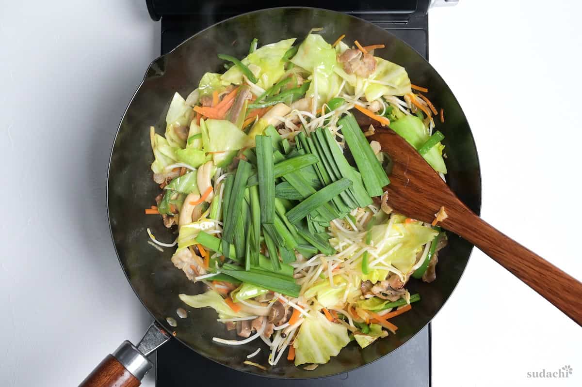 Garlic chives added to niku yasai itame frying in a wok on the stove top.