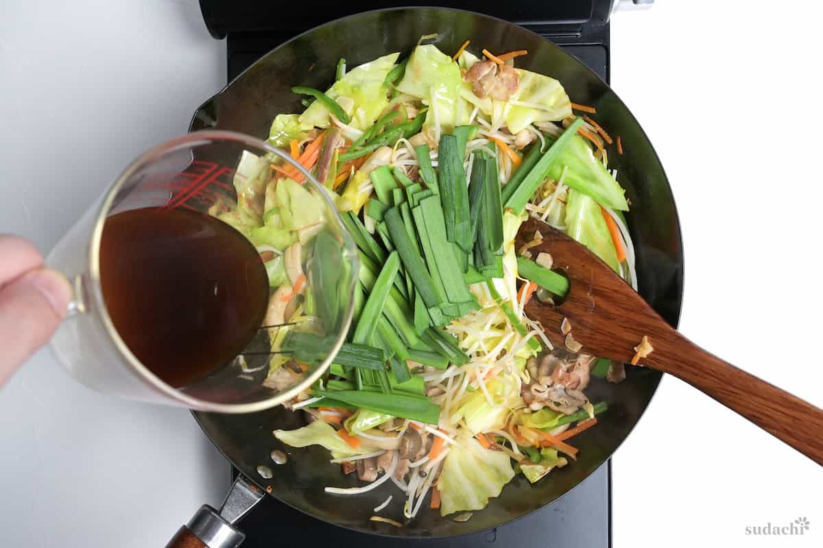 Pouring sauce over niku yasai itame in a wok on the stove top.