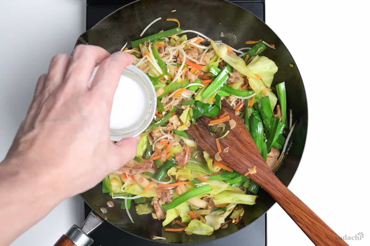 Pouring a slurry made with starch and water into a wok of niku yasai itame.