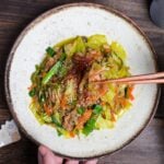 Niku Yasai Itame (Japanese meat and vegetable stir fry) topped with chili threads and sesame seeds on a cream plate with brown rim.