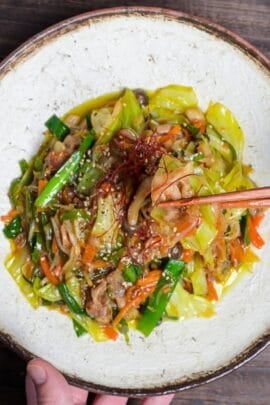 Niku Yasai Itame (Japanese meat and vegetable stir fry) topped with chili threads and sesame seeds on a cream plate with brown rim.