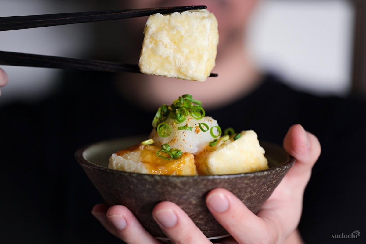 Yuto Omura holding up a piece of crispy tofu with chopsticks above a bowl of agedashi tofu