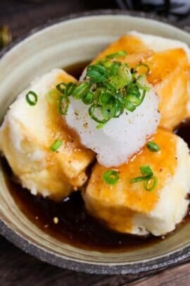 Agedashi tofu topped with grated daikon radish and chopped green onion in a cream ceramic bowl with brown rim