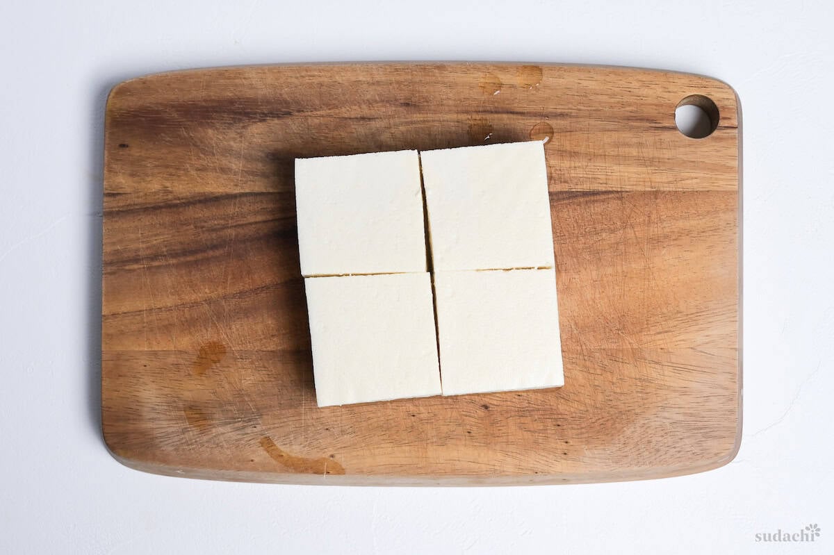 A block of firm tofu cut into 4 squares on a wooden cutting board