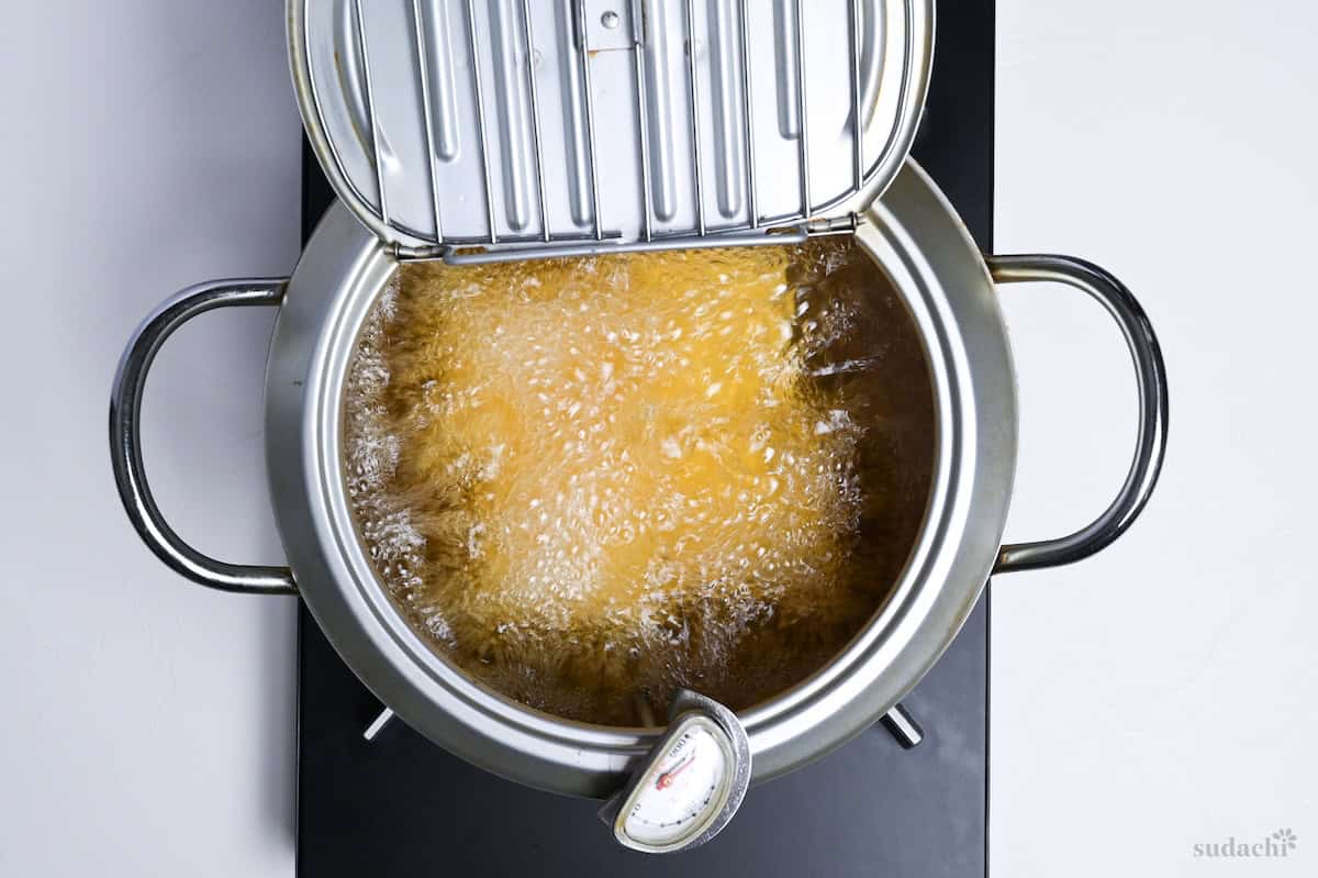 Four pieces of pressed firm tofu deep frying in a tempura pot to make atsuage tofu