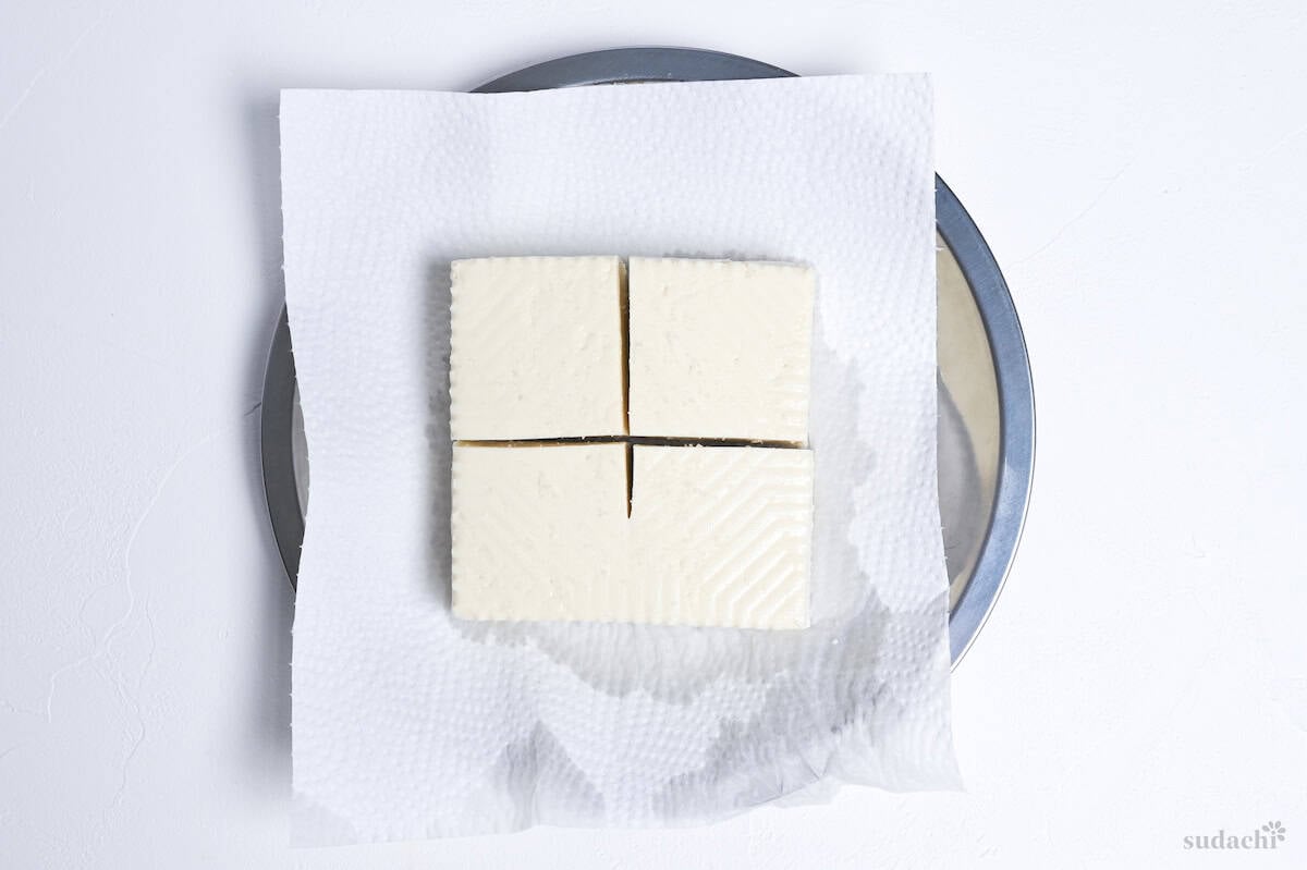 4 cubes of firm tofu on kitchen paper on a silver plate