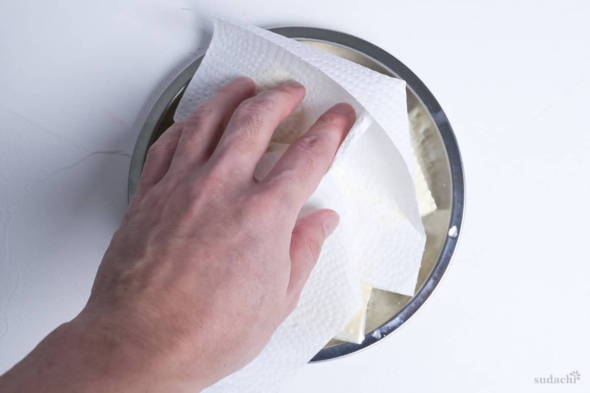 A hand pressing the surface of tofu with kitchen paper