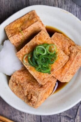 Four pieces of atsuage tofu in a cream bowl with dashi soy sauce and grated daikon radish