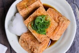 Four pieces of atsuage tofu in a cream bowl with dashi soy sauce and grated daikon radish