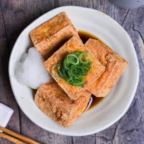 Four pieces of atsuage tofu in a cream bowl with dashi soy sauce and grated daikon radish