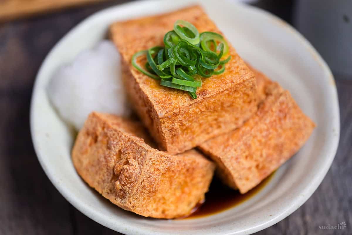 Four pieces of atsuage tofu in a cream bowl with dashi soy sauce and grated daikon radish