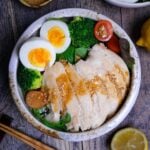 Pouring wafu dressing over salad chicken in a bowl with mixed leaf salad, boiled eggs. mini tomatoes and broccoli