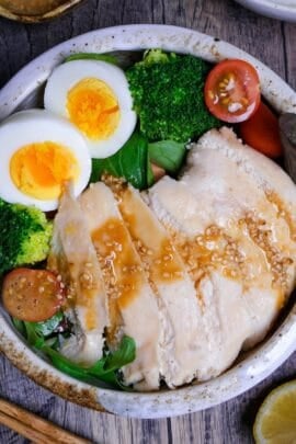 Pouring wafu dressing over salad chicken in a bowl with mixed leaf salad, boiled eggs. mini tomatoes and broccoli