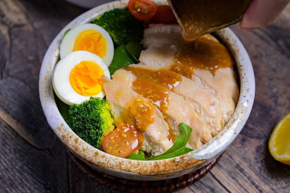 Japanese salad chicken being drizzled with wafu dressing in a small green jug