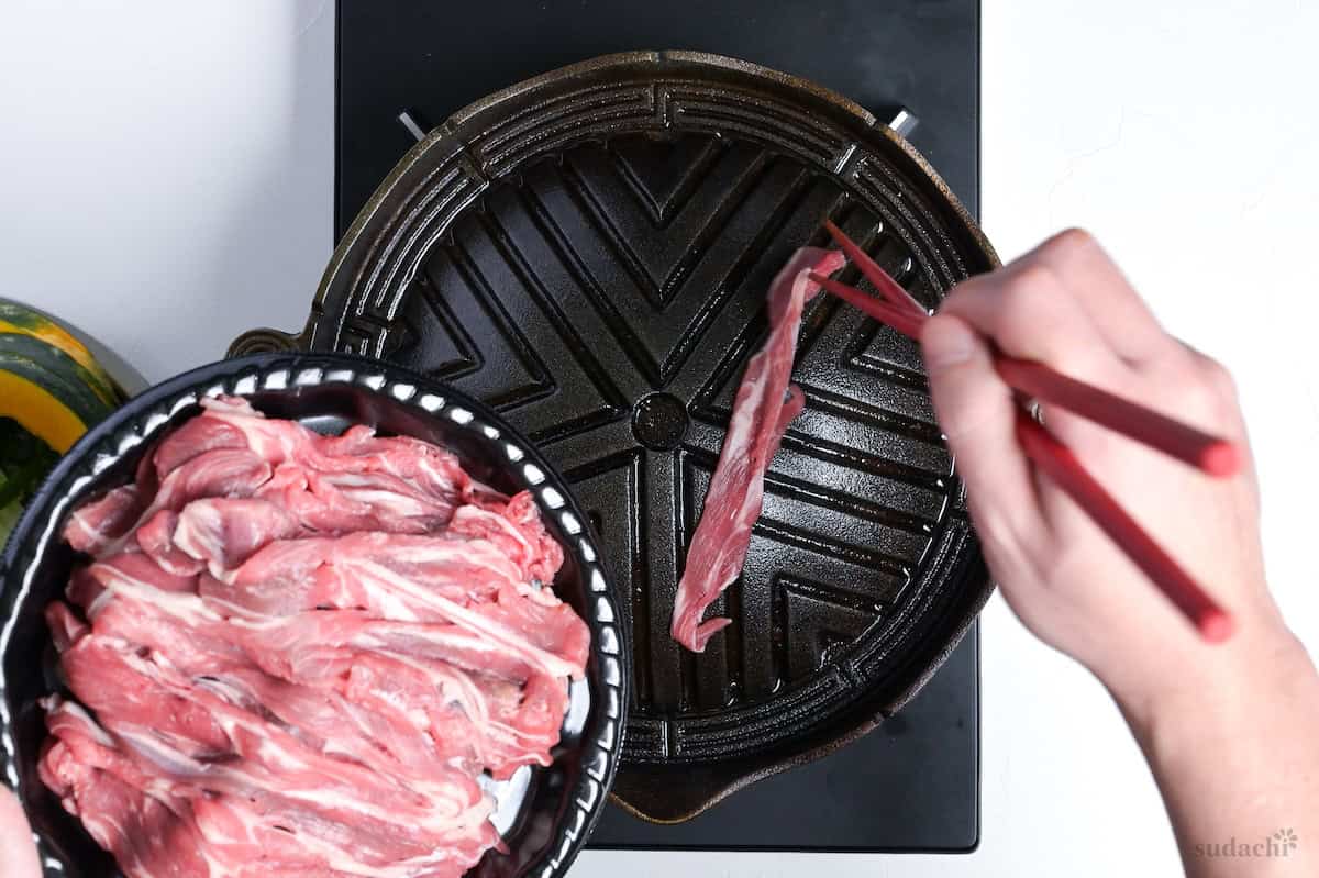 Placing thinly sliced lamb shoulder on a Mongolian BBQ griddle to make jingisukan