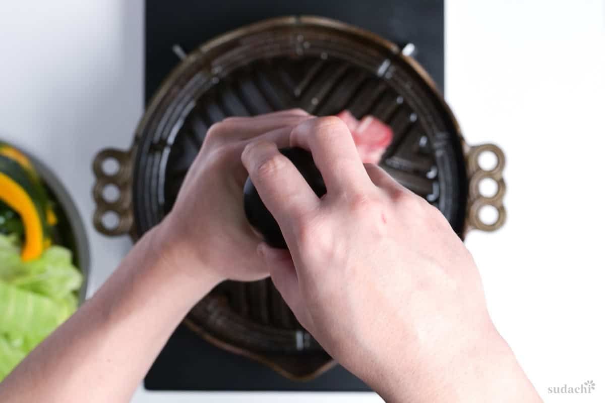 cracking coarse salt over thinly sliced lamb on a Mongolian BBQ grill for jingisukan