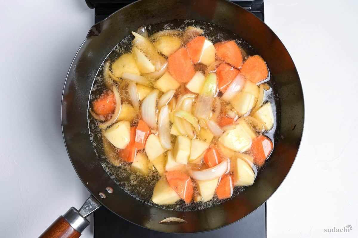 onions, carrots and dashi simmering in dashi broth in a large wok