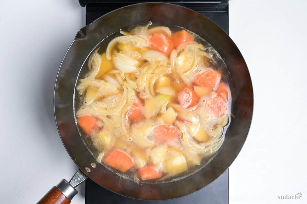 onions, carrots and dashi simmering in dashi broth in a large wok