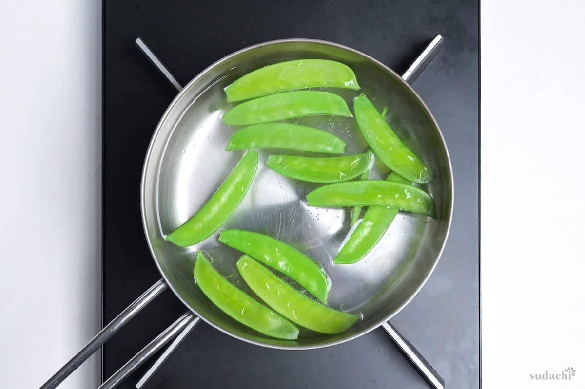 snow peas blanching in a small pot on the stove top