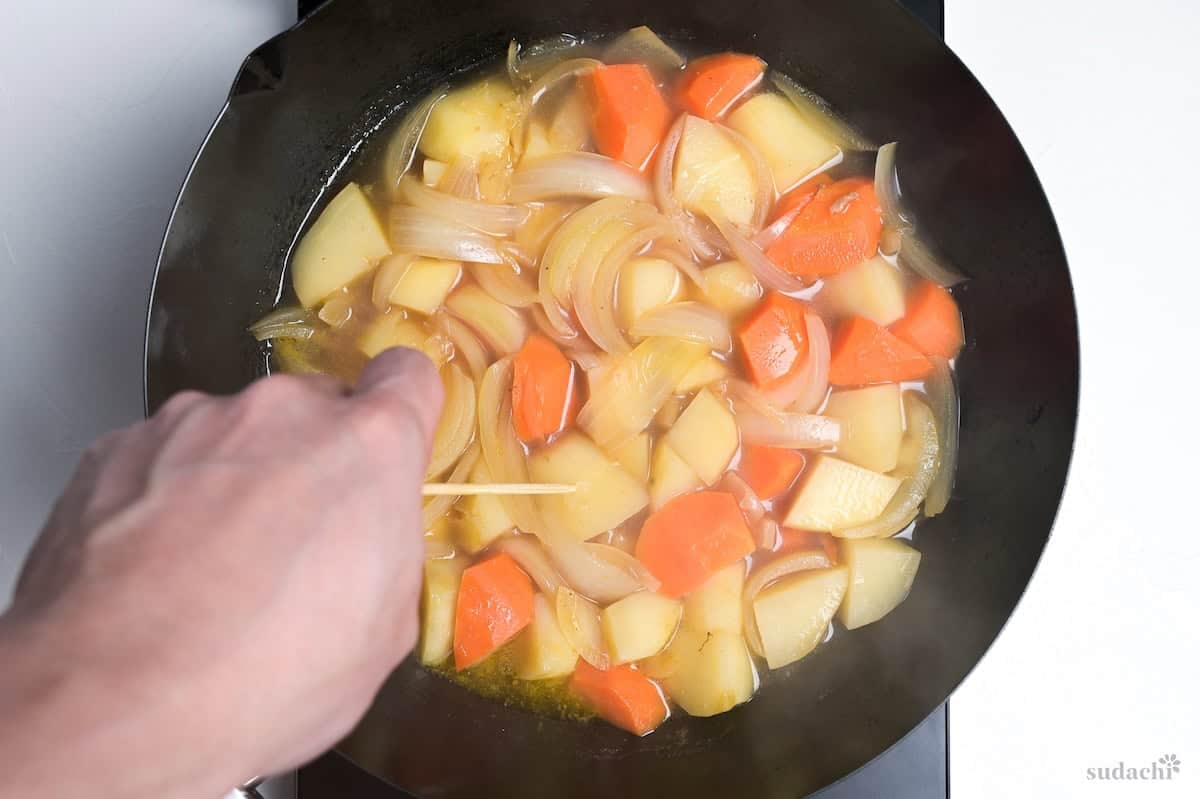 piercing potatoes with bamboo skewer in nikujaga to test doneness