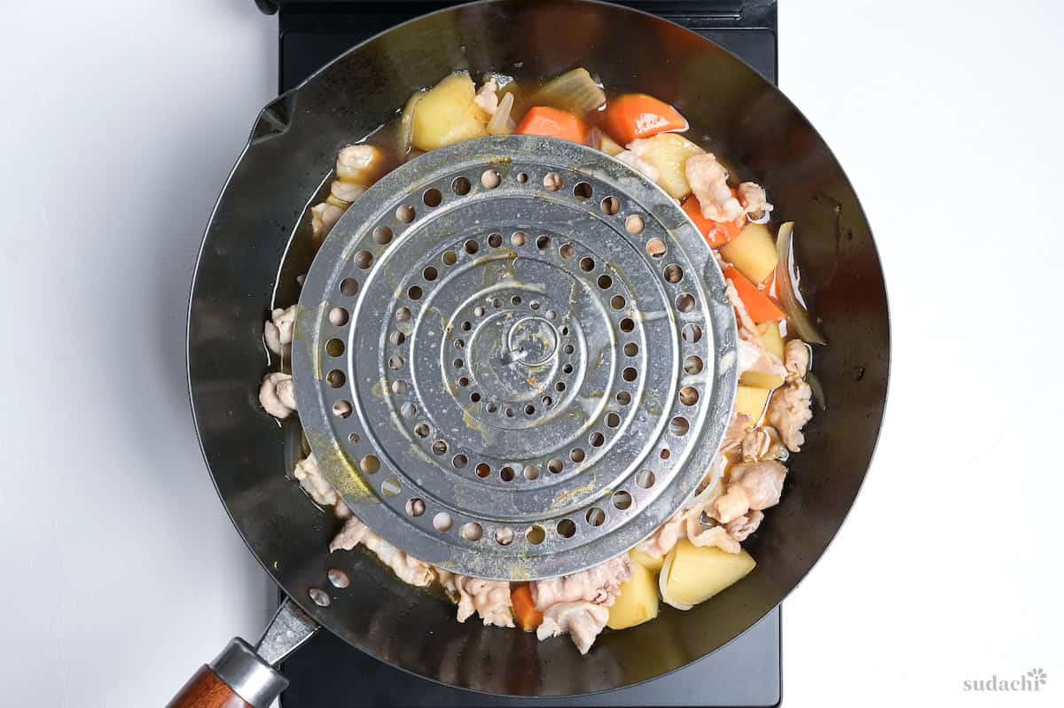 simmering nikujaga with a drop lid in a large wok on the stove top