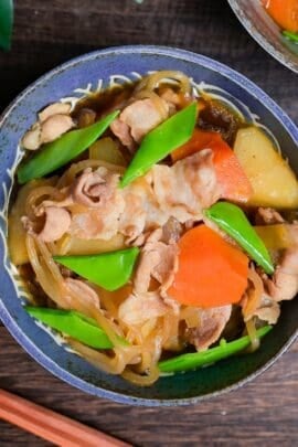 Nikujaga (Japanese meat and potato stew) with blanched snow peas in a blue bowl