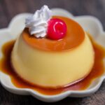 Japanese oven baked purin topped with whipped cream and a maraschino cherry on a flower shaped plate