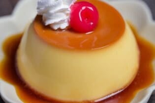 Japanese oven baked purin topped with whipped cream and a maraschino cherry on a flower shaped plate