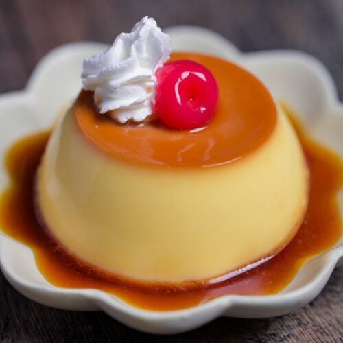 Japanese oven baked purin topped with whipped cream and a maraschino cherry on a flower shaped plate