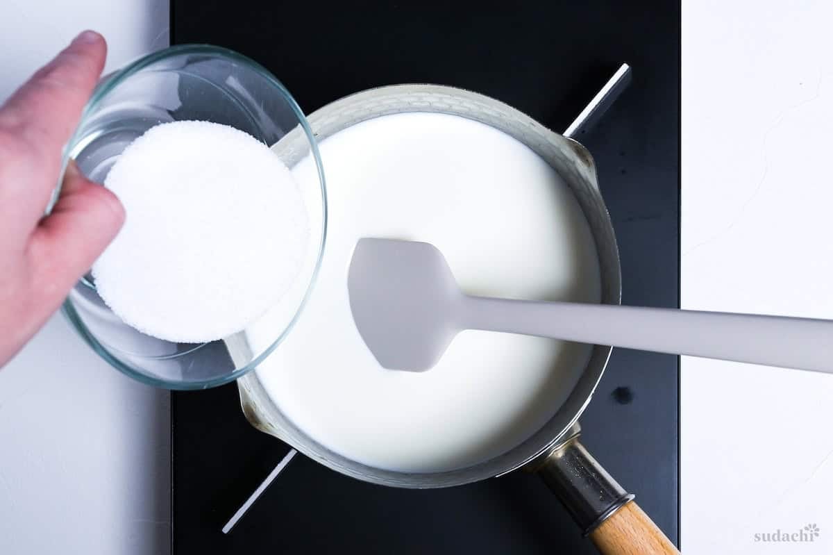 Pouring white sugar into heated cream and milk