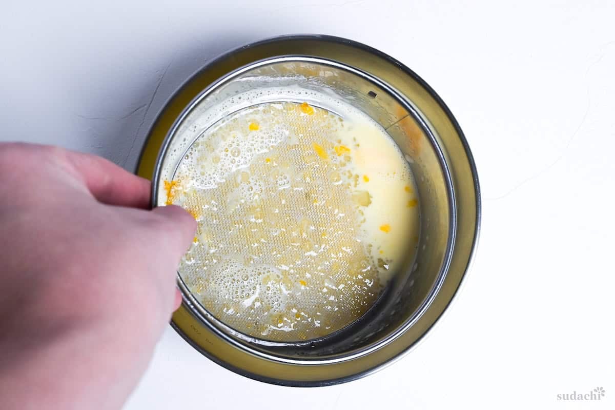 A sieve catching air bubbles, bits of egg yolk and egg white after straining purin mixture