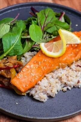 ponzu salmon on a bed of multigrain rice next to sautéed vegetables and baby leaf salad on a gray plate