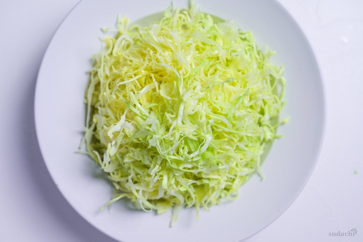 Shredded green cabbage in a white dish on a white background
