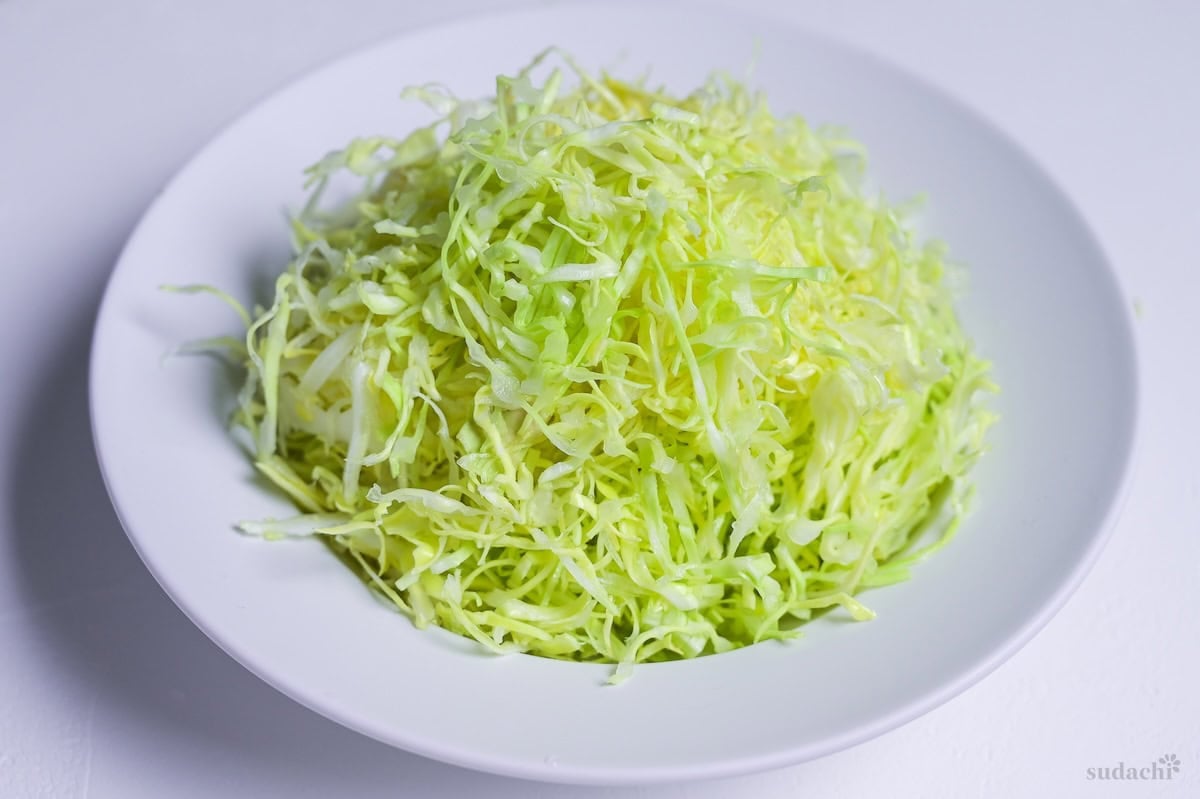 Shredded green cabbage in a white dish on a white background