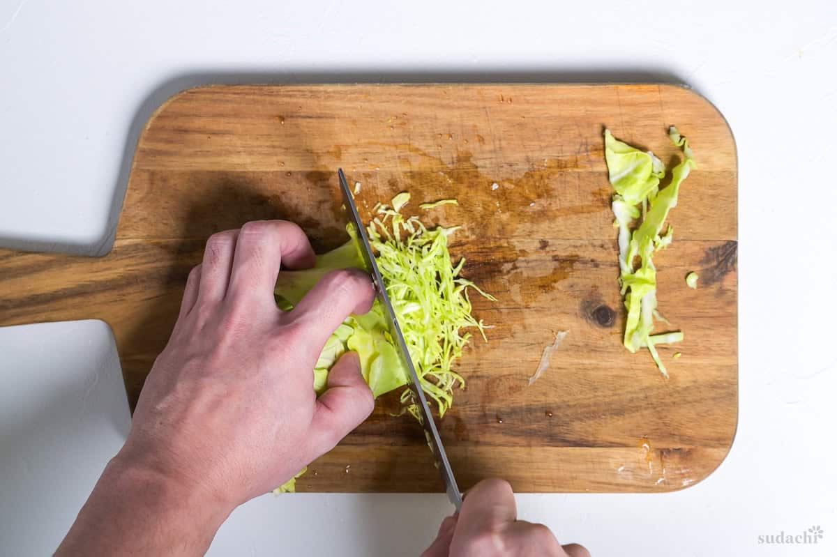 Thinly slicing (shredding) rolled cabbage leaves with knife on a wooden cutting board