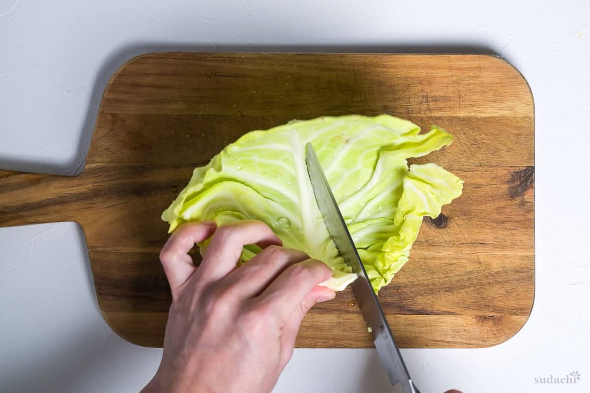Cutting thick stem out of cabbage leaf on a wooden cutting board