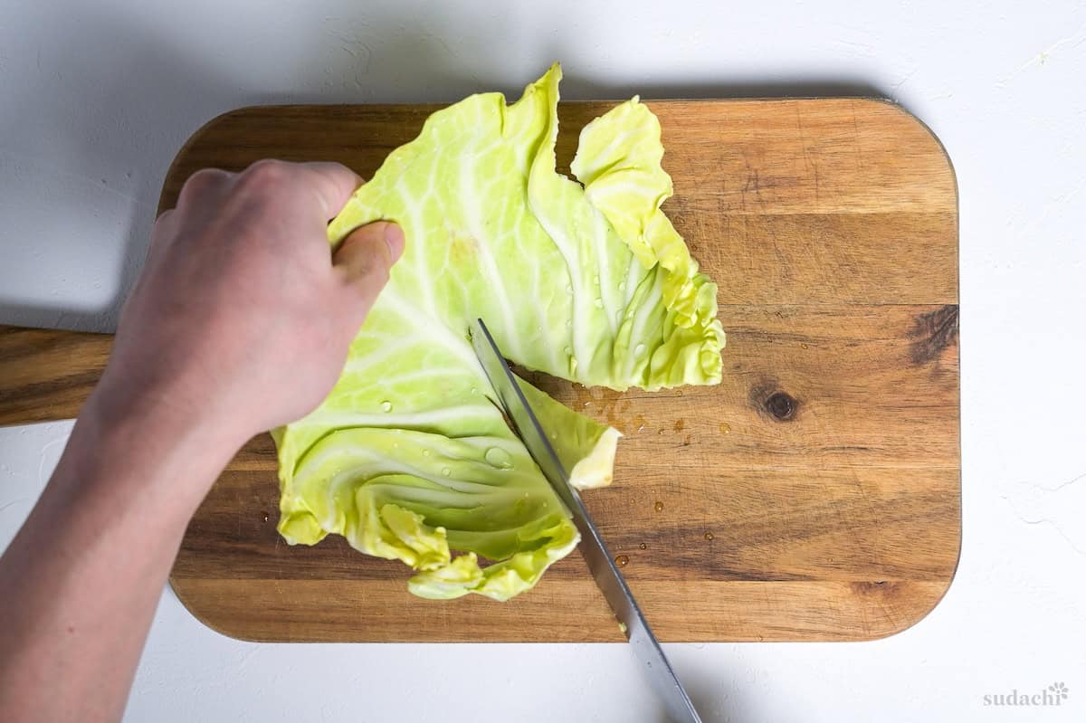 Cutting thick stem out of cabbage leaf on a wooden cutting board