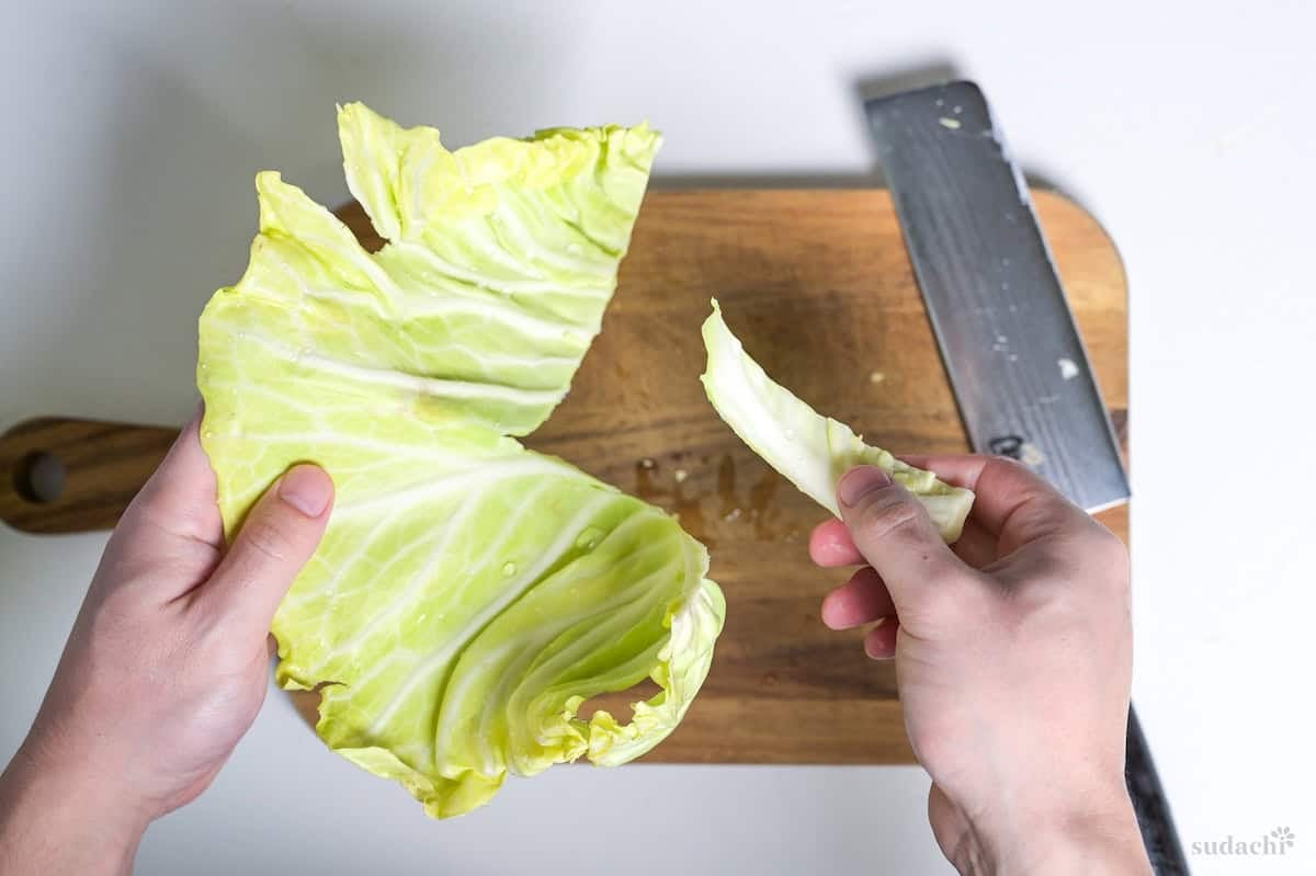 Cutting thick stem out of cabbage leaf on a wooden cutting board