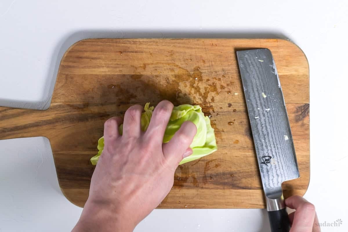 Cabbage leaves rolled up on a wooden cutting board ready for shredding