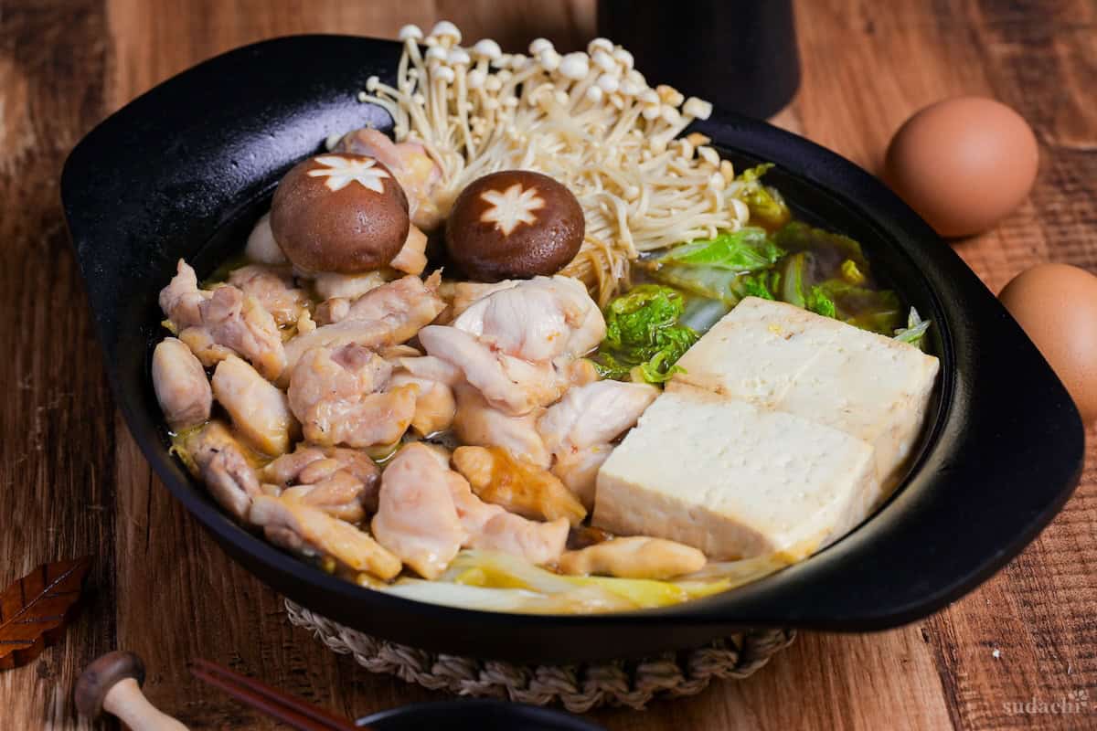Chicken sukiyaki with enoki mushrooms, shiitake, cabbage and tofu in a cast iron pot, wish eggs on the side